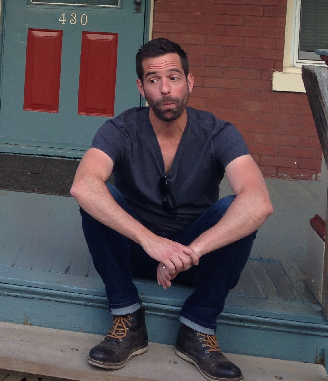 Man sitting on front steps outside a door, looking to the side with a thoughtful expression